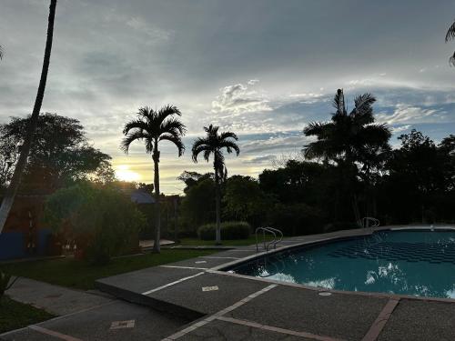 a swimming pool with palm trees and a cloudy sky at Finca La perla in Pavas