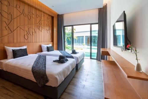 two beds in a hotel room with a tv and sliding glass doors at Tajh Pool Villas in Chalong 