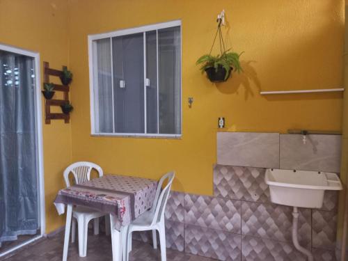 una mesa y sillas en una habitación amarilla con lavabo en Kitnet Arraial do Cabo, Monte Alto. en Arraial do Cabo