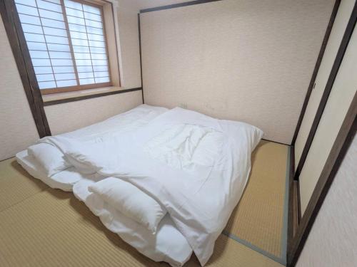 uma cama com lençóis brancos num quarto com uma janela em 1日1組限定の和室style心地よいコンドミニアム em Matsumoto