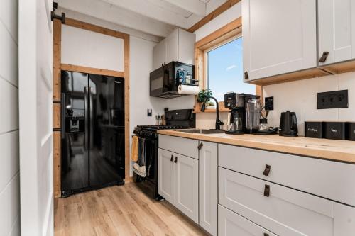 a kitchen with white cabinets and a black refrigerator at Modern Tiny Cabin, with Hot tub in Choteau MT in Choteau