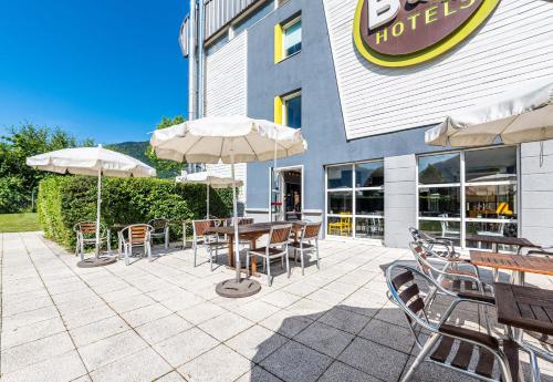 a patio with tables and chairs and umbrellas in front of a hotel at B&B HOTEL Saint Jean De Maurienne in Sainte-Marie-de-Cuines