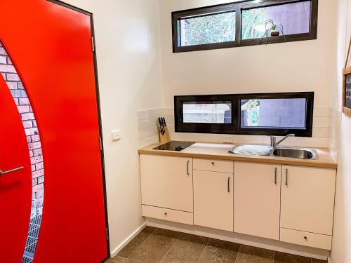 een keuken met een wastafel en een rode deur bij Tranquil Garden Studio with Stunning Lake Views in Ocean Grove