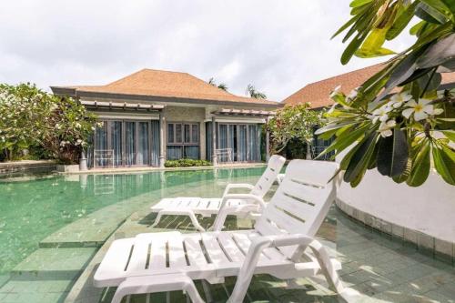 a group of white chairs sitting next to a swimming pool at Tajh Pool Villas in Chalong 