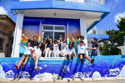 a group of people jumping in the air in front of a house at 交流型ゲストハウス伊良部ジャーニーインIrabu Joureny INN#毎日みんなで夕食会#ゲストさんは20-30代が中心#海徒歩1分#空港車で5分#本格フィンランドサウナ付き#海と星と夕日が見える屋上あり in Miyako-jima