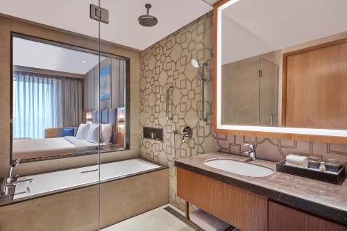 a bathroom with a sink and a shower and a bed at Doubletree By Hilton Varanasi in Varanasi
