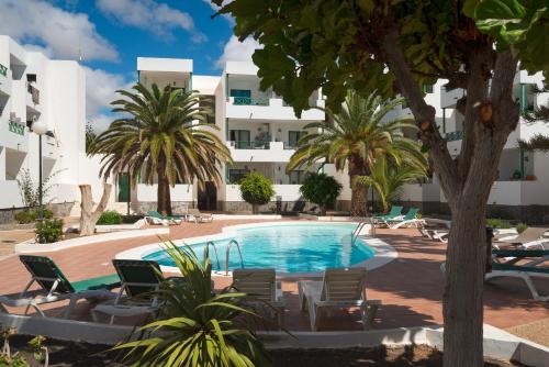 a pool with chairs and palm trees in front of a building at Lanzahost Carmenes Comfort in Costa Teguise
