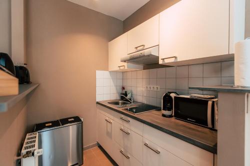 a kitchen with white cabinets and a sink and a microwave at Luga Homes - Chausseehaus in Leipzig