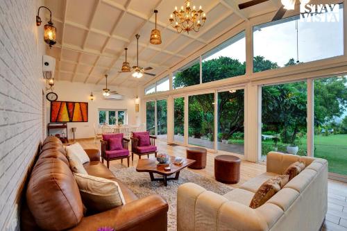 a large living room with leather furniture and large windows at StayVista at Idyllic Farmhouse - A Glasshouse with Outdoor Pool in Gurgaon