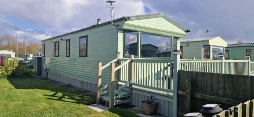 a green tiny house in a yard with a fence at Herons Mead Touring Park and Fishing Lakes - Plot 18 in Orby