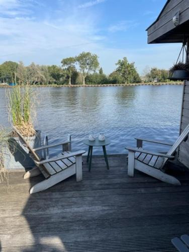 a dock with two chairs and a table next to a lake at Aangenaam op de Rijn, woonboot, inclusief privé sauna in Alphen aan den Rijn