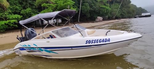 a white boat sitting on the water next to a beach at Lancha sossegada in Paraty