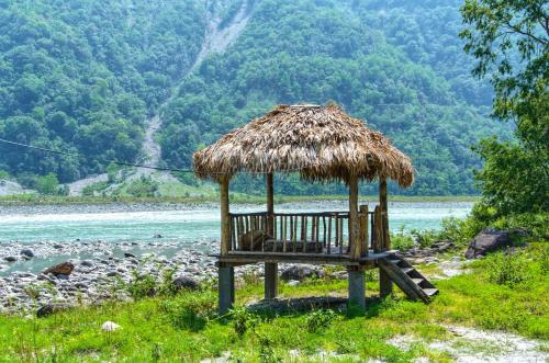 a bench with a straw hut next to a river at Beyond Brahmaputra & Eagles Nest 