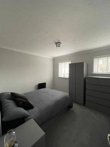 a bedroom with a bed and a dresser and two windows at Eaton Ford Green Ground Floor Apartment in Saint Neots