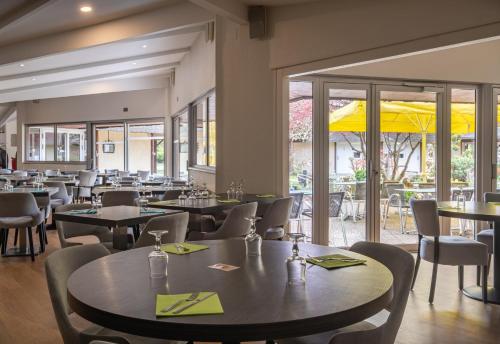 a restaurant with tables and chairs and windows at Charme Hôtel, Montbéliard Sud in Montbéliard