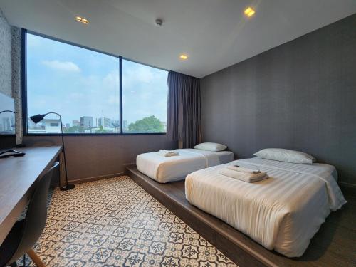 a hotel room with two beds and a desk and window at Happy Station Bangkok in Bangkok