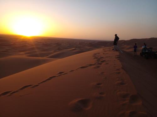 um grupo de pessoas em pé sobre uma duna de areia no deserto em Merzouga Chebbi camp em Adrouine