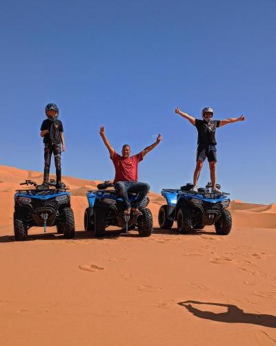three men standing on atvs in the desert at Merzouga Chebbi camp in Hassilabied