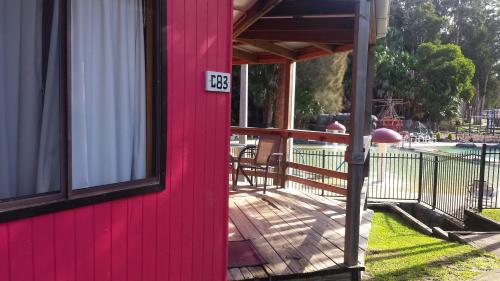 a red house with a deck next to a pool at Smugglers Cove Holiday Village in Forster