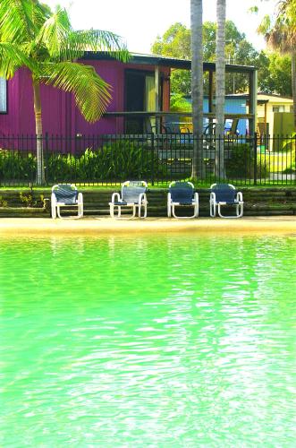 four chairs sitting on a beach next to the water at Smugglers Cove Holiday Village in Forster