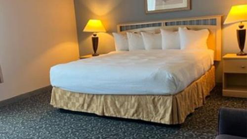 オーシャン・ショアーズにあるLighthouse Suites Innの白い大型ベッド(ランプ2つ付)が備わる客室です。