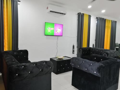ein Wohnzimmer mit zwei schwarzen Stühlen und einem TV in der Unterkunft Marvelous Homestay SP Kedah in Sungai Petani