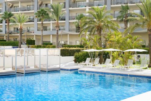 a swimming pool with chairs and umbrellas in front of a building at Zafiro Palace Alcudia in Port d'Alcudia
