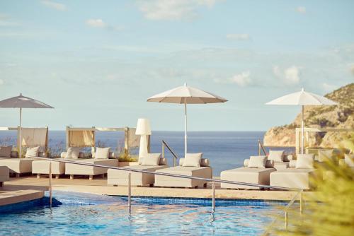 a pool with white chairs and umbrellas next to the ocean at Zafiro Palace Andratx in Camp de Mar