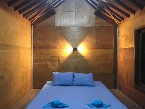 a bed in a room with a light on the wall at Muni's Lombok Bungalow in Masbagik