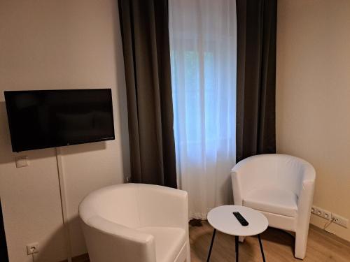 a room with two white chairs and a flat screen tv at Hotel Zum Postkutscher in Cottbus