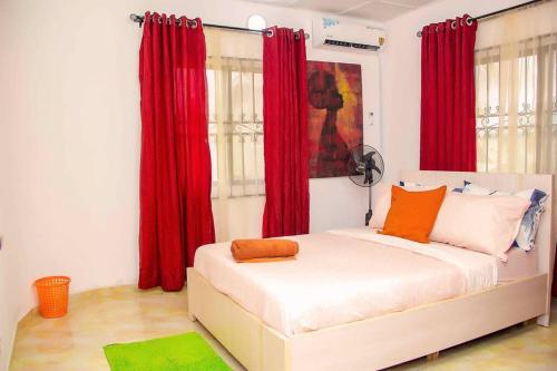 a bedroom with red curtains and a white bed with orange pillows at ARO (1.0) 2BD Studio Flat (Abule-Egba/Lagos) in Agege