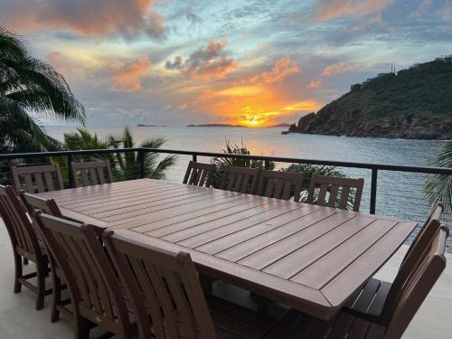 a wooden table and chairs on a balcony with a sunset at Lime in de Coconut Villa in Cruz Bay