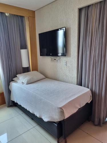 a bedroom with a bed with a flat screen tv on the wall at Condomínio Tower Cobertura 1503 in Belo Horizonte