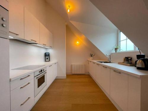 une cuisine mansardée avec des placards blancs et un escalier dans l'établissement Grand appartement renové centre historique proche plages, à Perros-Guirec