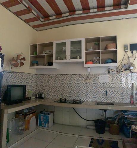 a kitchen with white cabinets and a tv on a wall at Butterfly Kost Tulungagung in Ngantru