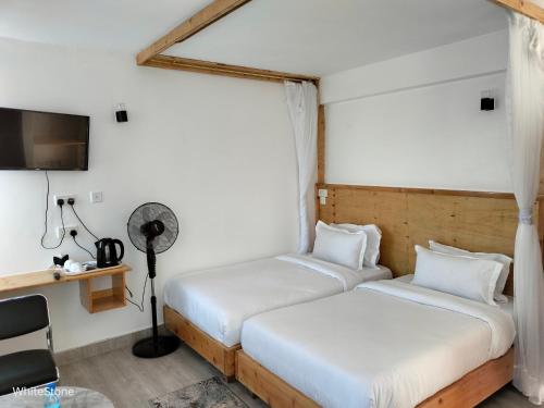 Habitación con 2 camas, escritorio y TV. en White Stone Beach Resort, en Mbita