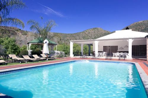 a swimming pool with chairs and a house at Old Mill Lodge, Seasonal Working Ostrich Farm & Restaurant, Oudtshoorn in Oudtshoorn