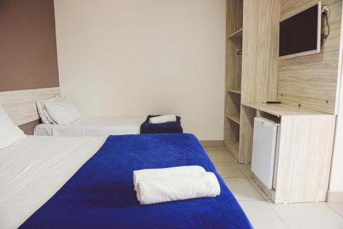 a hotel room with a blue and white bed and a tv at Pousada Xerxes in Arraial do Cabo