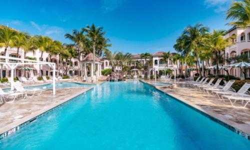 a pool at a resort with chairs and palm trees at Caribbean Palm Village Resort in Palm-Eagle Beach