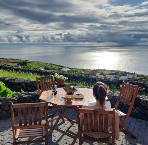 a woman sitting at a table with a view of the ocean at Ti Chôa - Casa do Biscoitinho in Angra do Heroísmo