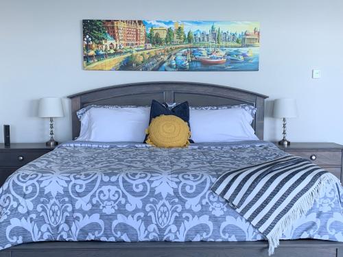 a bed with a blue and white comforter and a painting at Ocean Front Private Suite in Victoria