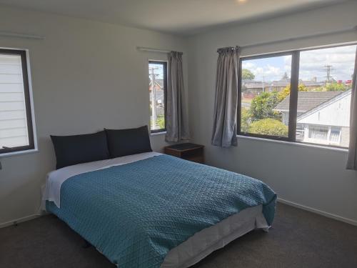 um quarto com uma cama azul e 2 janelas em Lovely House in Central Papatoetoe em Auckland