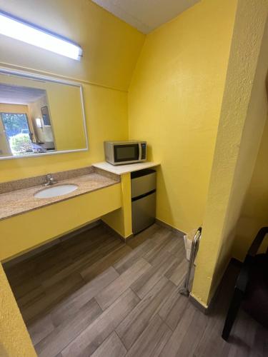 ein gelbes Badezimmer mit einem Waschbecken und einer Mikrowelle in der Unterkunft Hallmarc Inn in New Albany