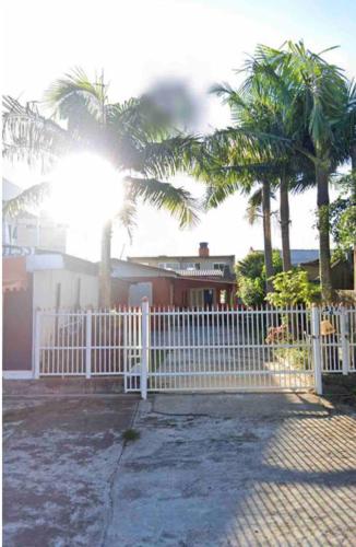 a white fence in front of a house with palm trees at Casa praia da cal in Torres