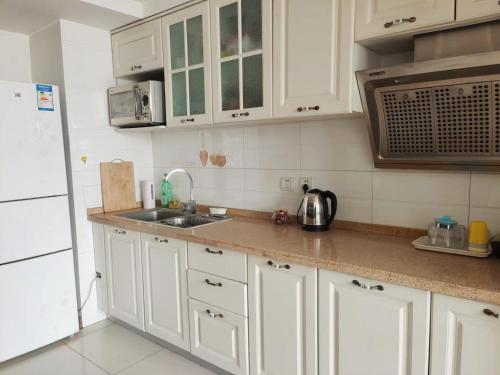 a kitchen with white cabinets and a sink and a refrigerator at Chaoyang Joy City Hardcover Apartment in Beijing