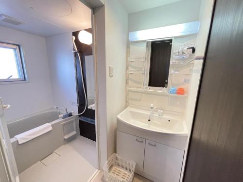 biała łazienka z umywalką i wanną w obiekcie BiBi Hotel FUTENMA w mieście Ginowan