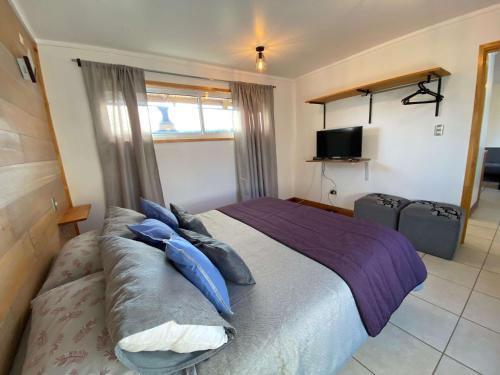 a bedroom with a bed with blue pillows and a television at Cabaña Clásica - BBQ Cocina Estacionamiento Wifi in Quintay