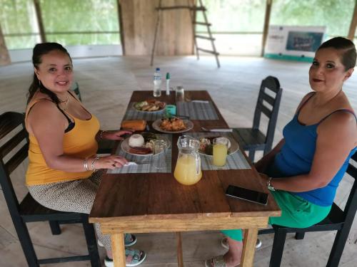 zwei Frauen sitzen an einem Holztisch mit Essen in der Unterkunft Canoa Inn Natural Lodge in Iquitos