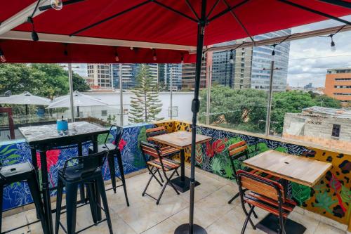 eine Terrasse mit Tischen, Stühlen und einem roten Regenschirm in der Unterkunft Usaquen Station Hostel in Bogotá
