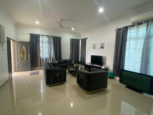 sala de estar con muebles negros y TV de pantalla plana en EMPIRE HOMESTAY PAKA ROOM 2, en Paka